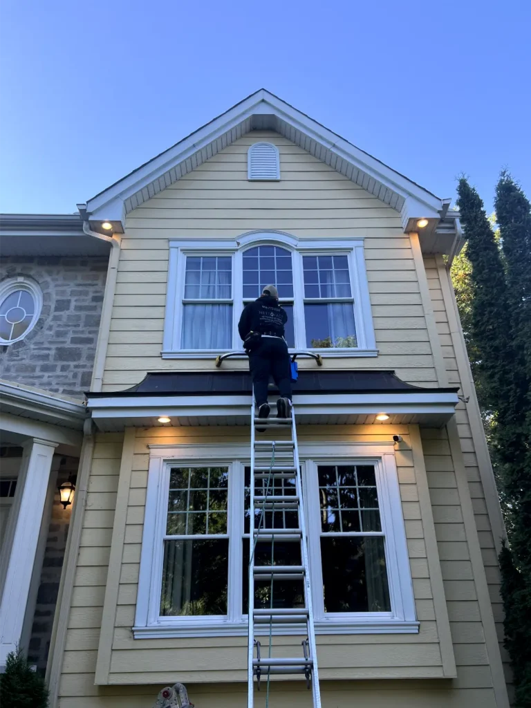 Technician cleaning residential windows on a ladder, showcasing professional window maintenance services by Ö Nettoyage in Greater Montreal.